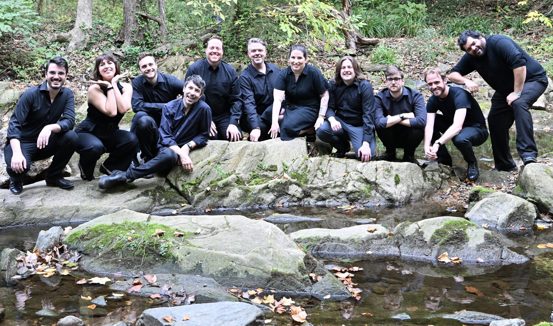 Ensemble members pose together beside a creek